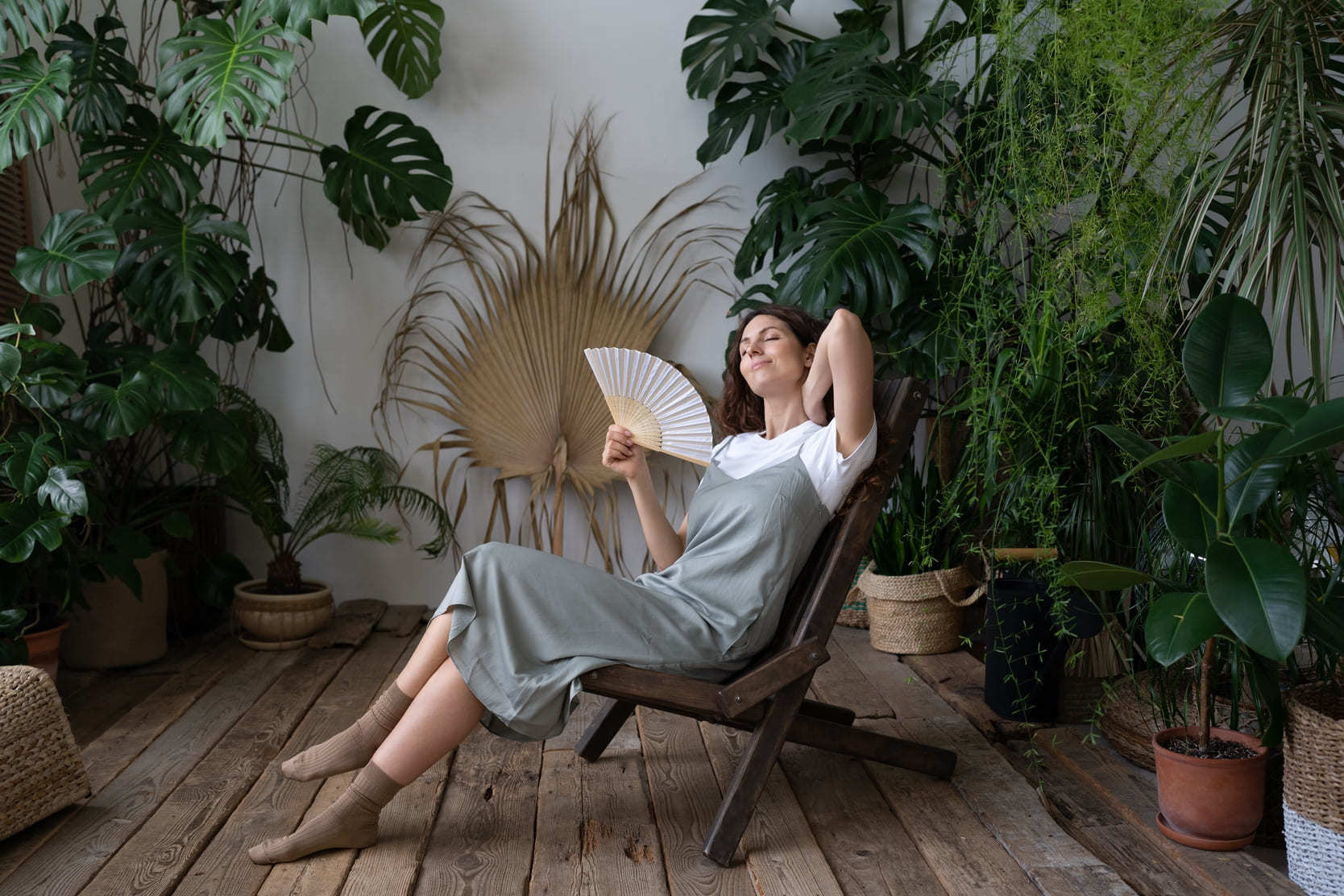 Woman cooling off with a fan in a plant-filled room